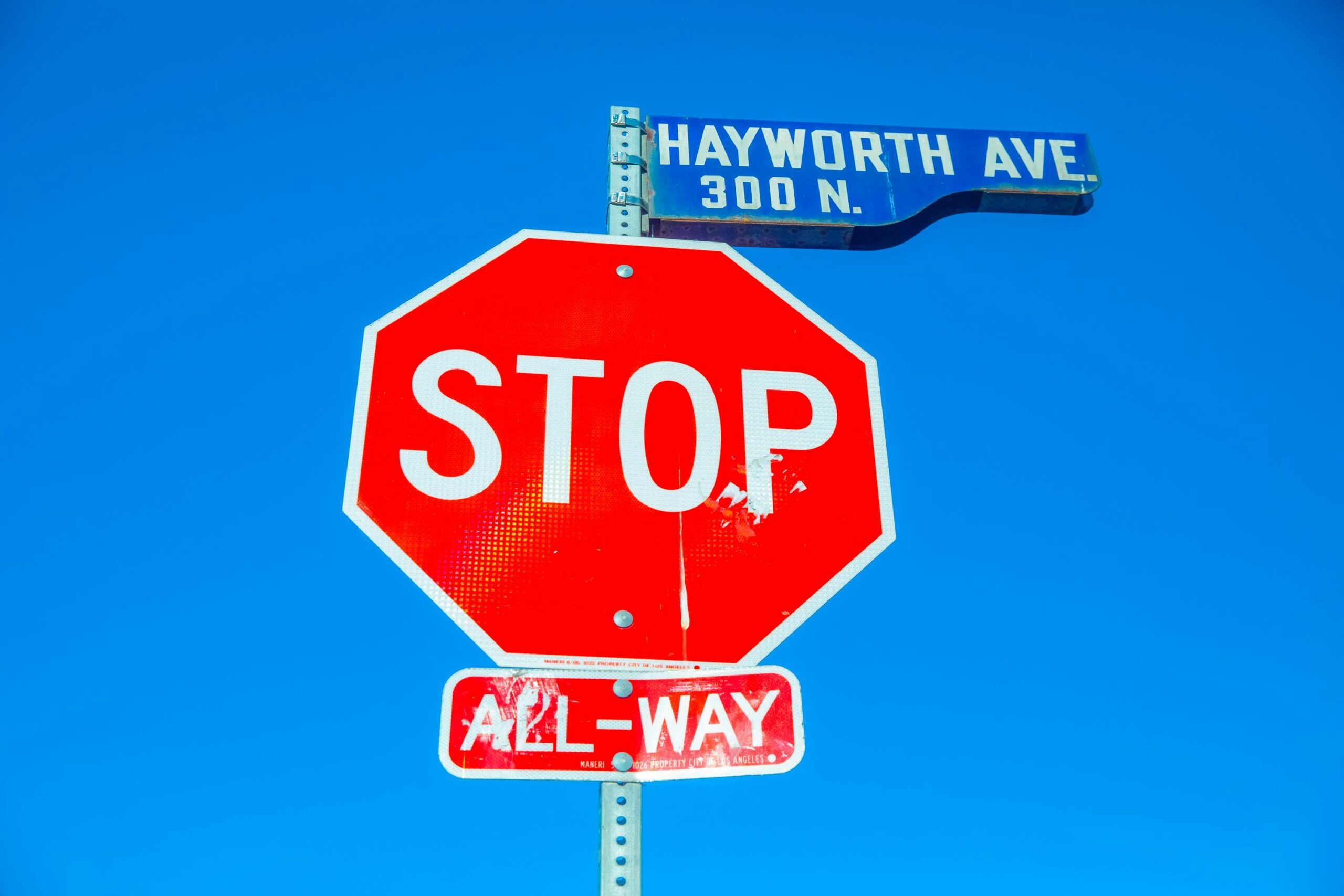 Colorful stop sign at Hayworth Ave intersection against a clear blue sky.